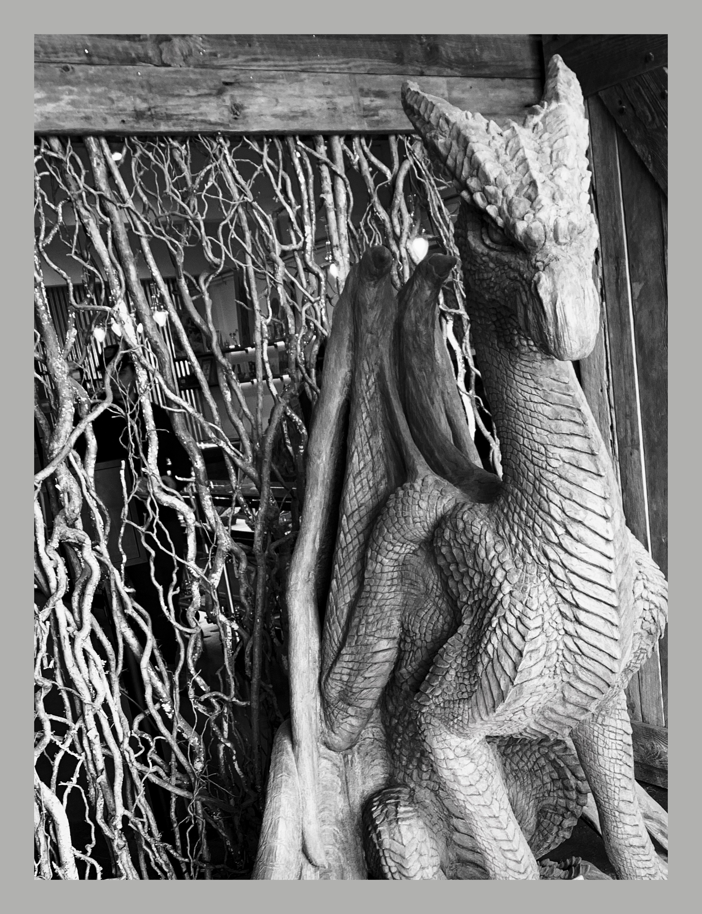 Black-and-white photo of a carved wooden dragon in front of a wall of twisted branches